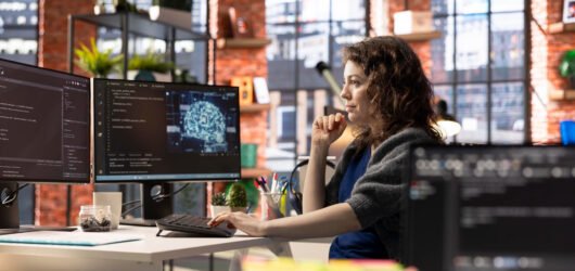 Desenvolvedora de software trabalhando em um ambiente corporativo com múltiplos monitores exibindo código, inteligência artificial e aplicações empresariais.