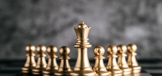 Rainha dourada de xadrez à frente de outras peças, simbolizando liderança estratégica, planejamento e tomada de decisão em consultoria de tecnologia.