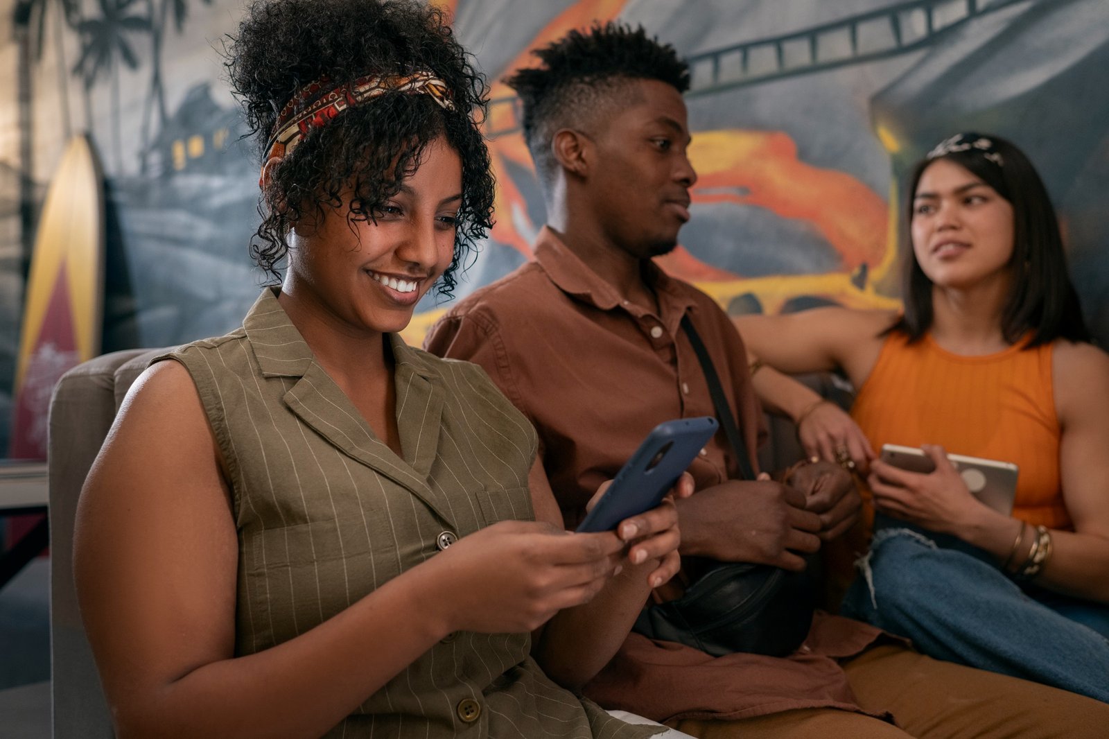 Mulher sorrindo enquanto utiliza um smartphone, ao lado de um homem sentado em ambiente interno.